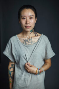 in this example of portrait photography you see a photography taken by jeff fried of a female Chinese citizen with many visible tattoos on her arms, chest and neck