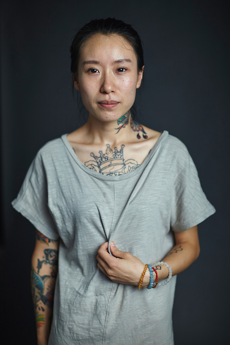 in this example of studio portrait photography you see a photograph taken by jeff fried of a female Chinese citizen with many visible tattoos on her arms, chest and neck, using hard light