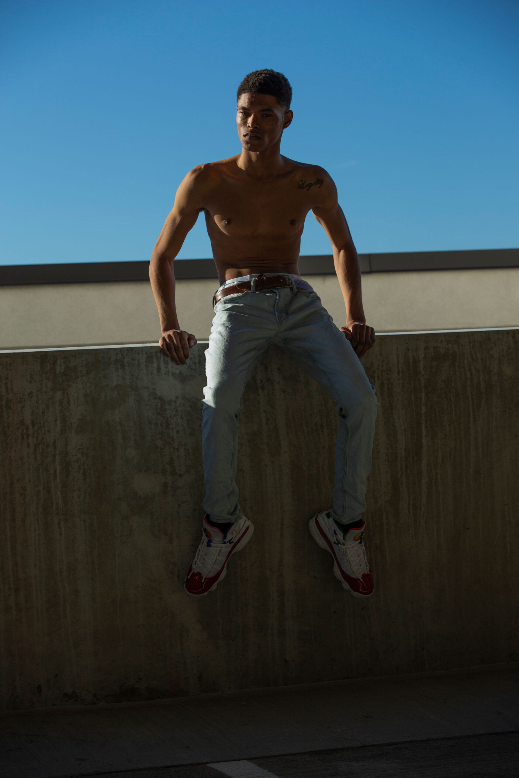 young posing man with no shirt while he sits on a concrete ledge